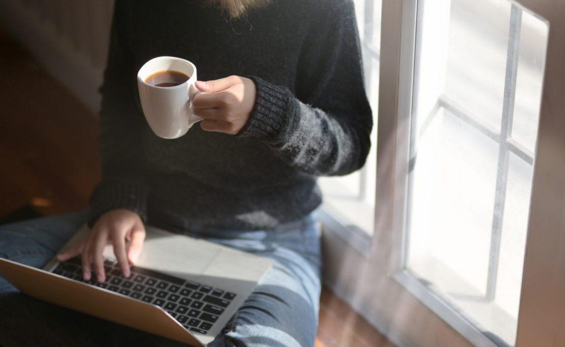 woman-using-laptop-while-holding-a-cup-of-coffee-3759083